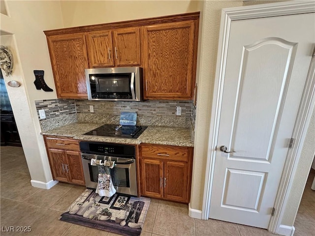 kitchen with appliances with stainless steel finishes, light tile patterned flooring, brown cabinetry, and tasteful backsplash