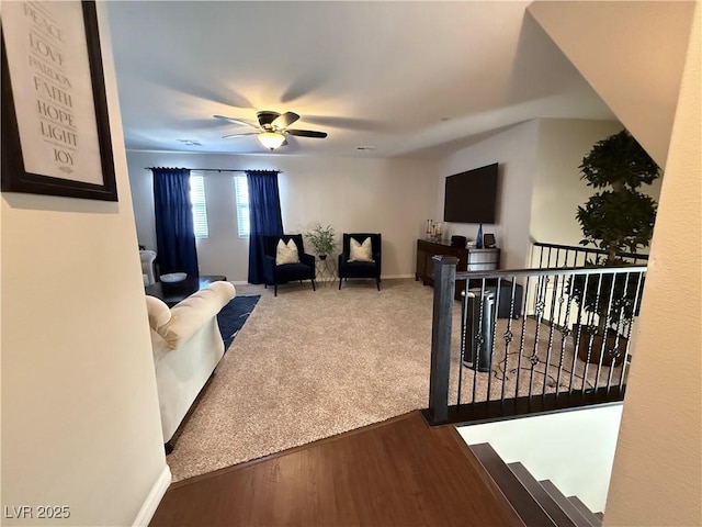 carpeted living area with visible vents, ceiling fan, baseboards, and wood finished floors