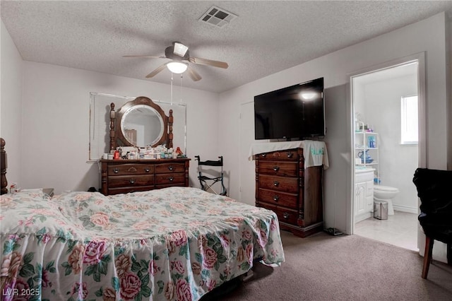 carpeted bedroom featuring a textured ceiling, a ceiling fan, visible vents, and ensuite bathroom