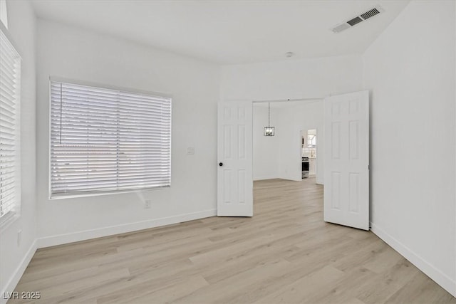 unfurnished room featuring baseboards, visible vents, and light wood-style floors