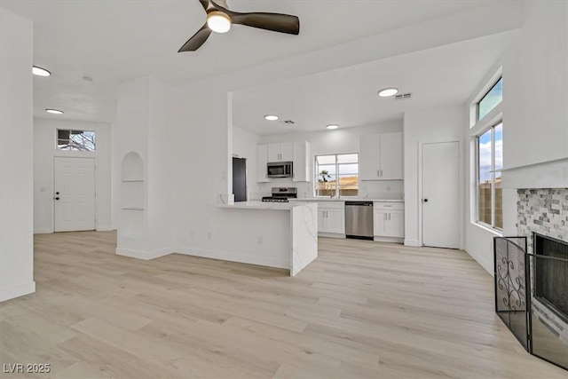 kitchen with light wood-style flooring, a fireplace, white cabinets, light countertops, and appliances with stainless steel finishes