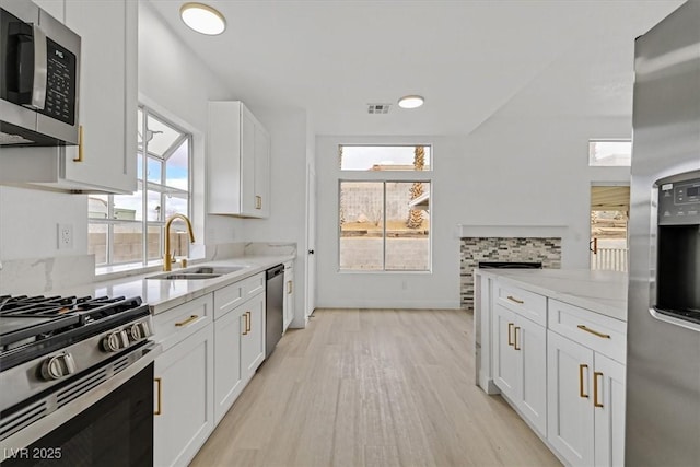 kitchen with visible vents, white cabinets, light stone counters, stainless steel appliances, and a sink