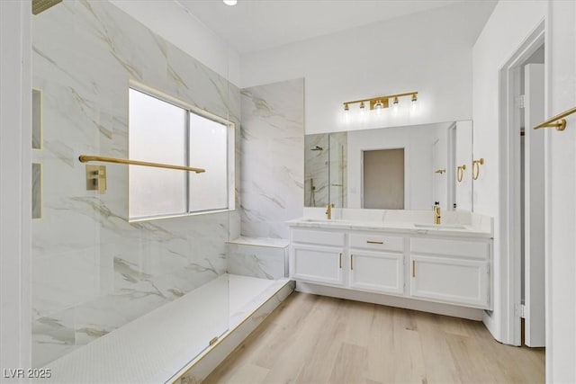 bathroom featuring double vanity, a sink, a marble finish shower, and wood finished floors