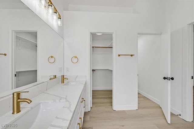 full bathroom featuring double vanity, a spacious closet, a sink, and wood finished floors