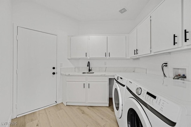 clothes washing area with a sink, visible vents, cabinet space, light wood finished floors, and washer and clothes dryer