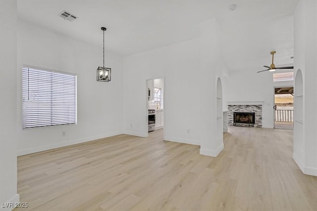 unfurnished living room featuring a wealth of natural light, arched walkways, visible vents, and ceiling fan with notable chandelier