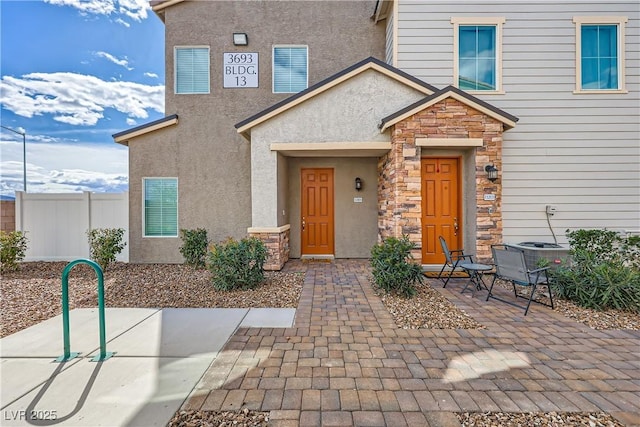 entrance to property featuring stone siding, fence, and stucco siding