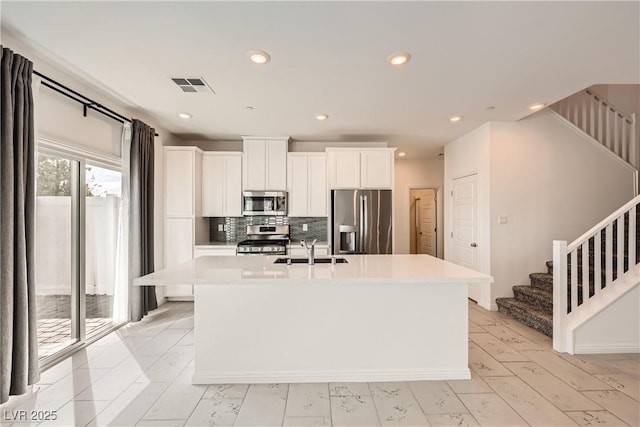 kitchen featuring visible vents, white cabinets, appliances with stainless steel finishes, a kitchen island with sink, and a sink