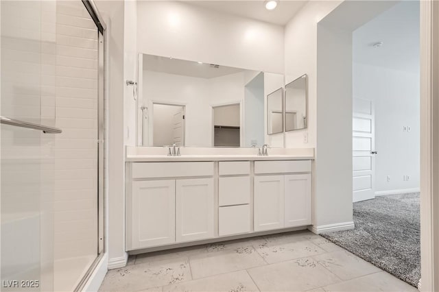 full bathroom with double vanity, a shower stall, baseboards, and a sink