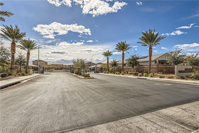 view of street with a gated entry, sidewalks, curbs, a residential view, and street lighting