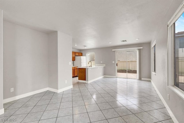 unfurnished living room with light tile patterned floors, a sink, visible vents, and baseboards