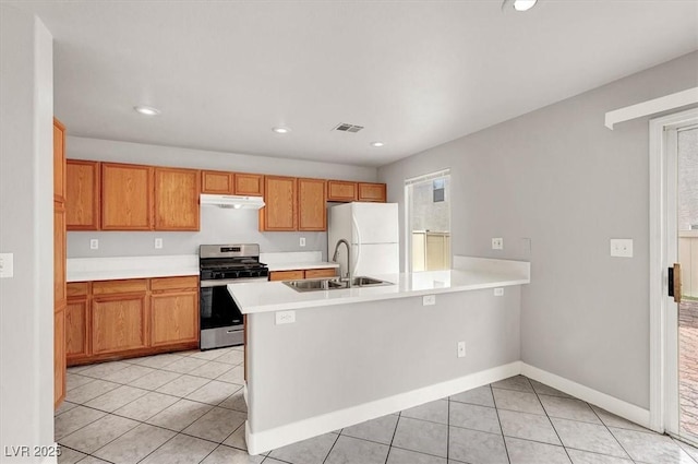 kitchen featuring under cabinet range hood, a peninsula, a sink, freestanding refrigerator, and stainless steel gas stove