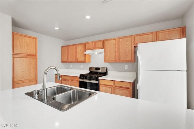 kitchen featuring light countertops, freestanding refrigerator, stainless steel gas stove, a sink, and under cabinet range hood