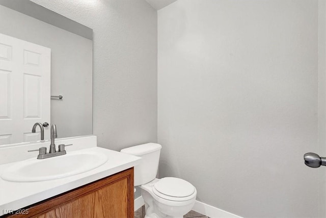 half bath with vanity, toilet, and baseboards