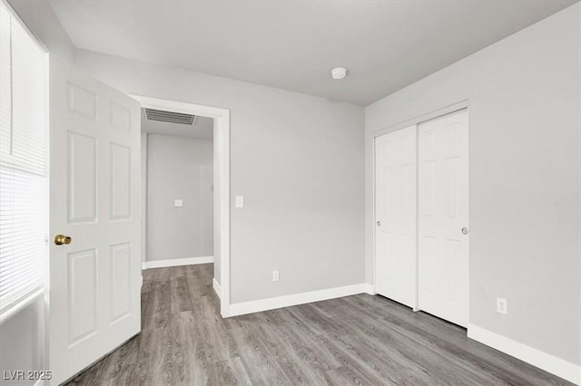 unfurnished bedroom featuring a closet, visible vents, baseboards, and wood finished floors