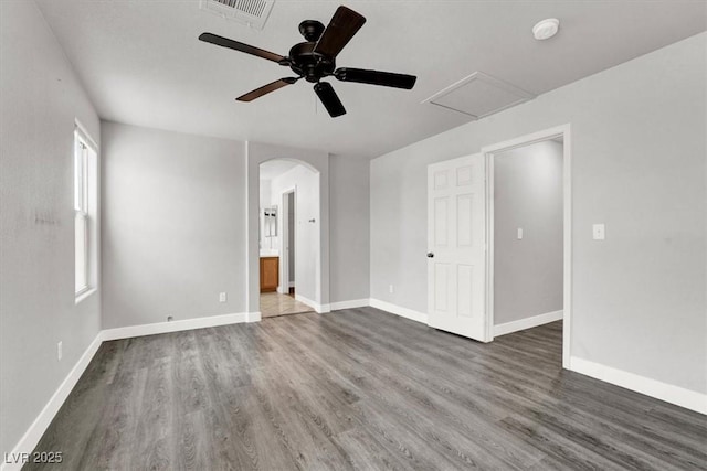 unfurnished bedroom with baseboards, visible vents, arched walkways, and wood finished floors