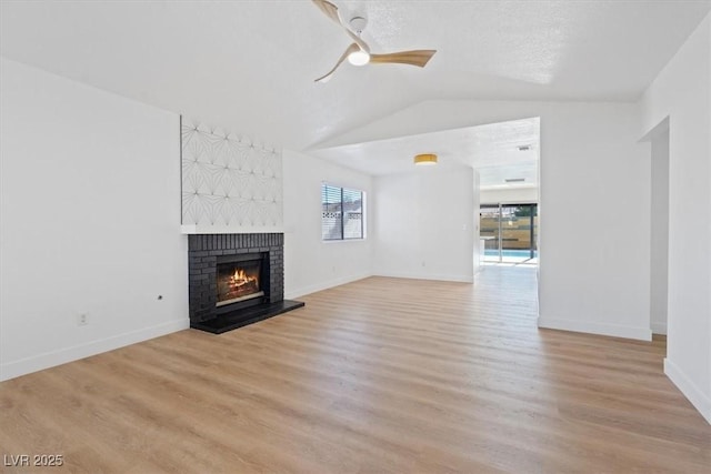 unfurnished living room featuring light wood-style flooring, a brick fireplace, vaulted ceiling, ceiling fan, and baseboards