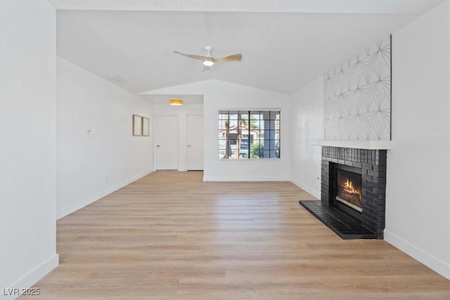 unfurnished living room with ceiling fan, light wood-style flooring, baseboards, vaulted ceiling, and a brick fireplace