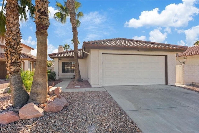 mediterranean / spanish house featuring a tile roof, a chimney, stucco siding, an attached garage, and driveway