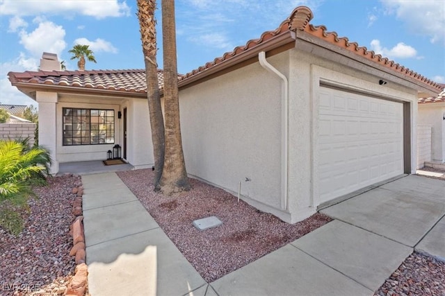 view of property exterior with concrete driveway, a tile roof, a chimney, an attached garage, and stucco siding