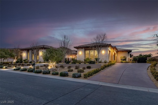 mediterranean / spanish home featuring stone siding, a tile roof, and driveway