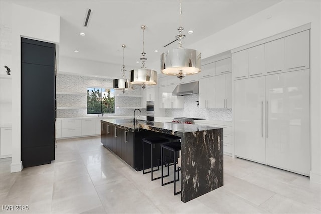 kitchen featuring under cabinet range hood, decorative backsplash, a sink, and decorative light fixtures