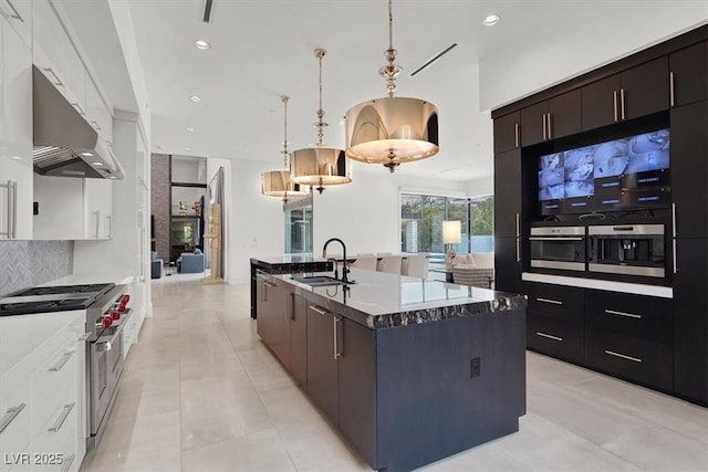 kitchen featuring decorative backsplash, open floor plan, a kitchen island with sink, under cabinet range hood, and a sink