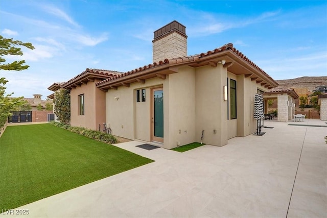 back of house featuring a patio, a lawn, a tile roof, and stucco siding