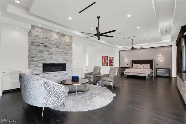 living area with wood finished floors, a tiled fireplace, a raised ceiling, and visible vents