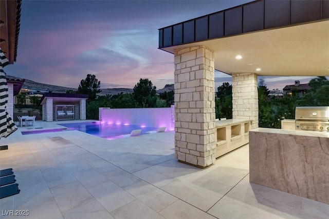 pool at dusk with an outdoor pool, a fireplace, a patio, and area for grilling