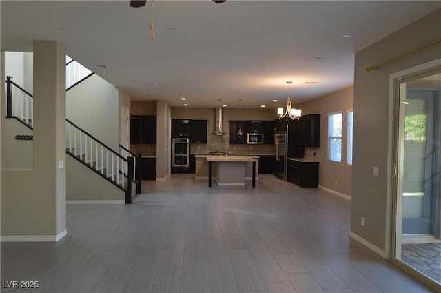 unfurnished living room with recessed lighting, stairway, baseboards, and ceiling fan with notable chandelier