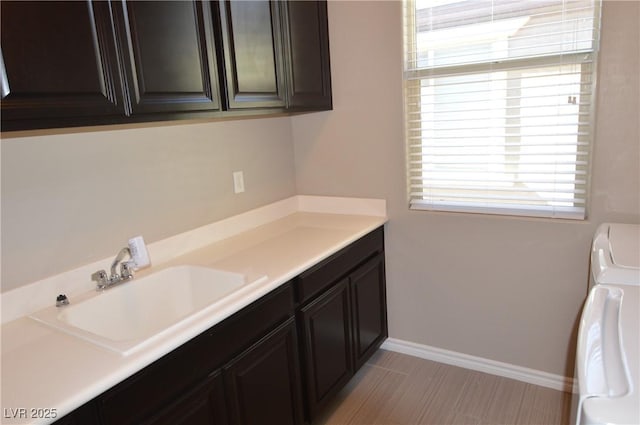 clothes washing area with independent washer and dryer, a sink, cabinet space, and baseboards