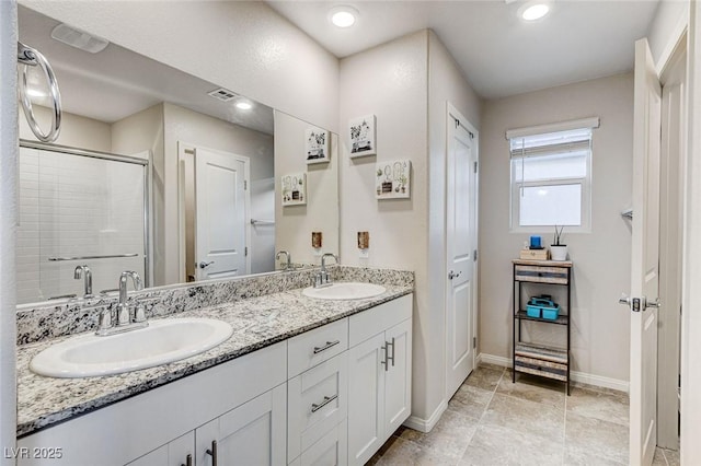 full bath featuring double vanity, a stall shower, baseboards, and a sink