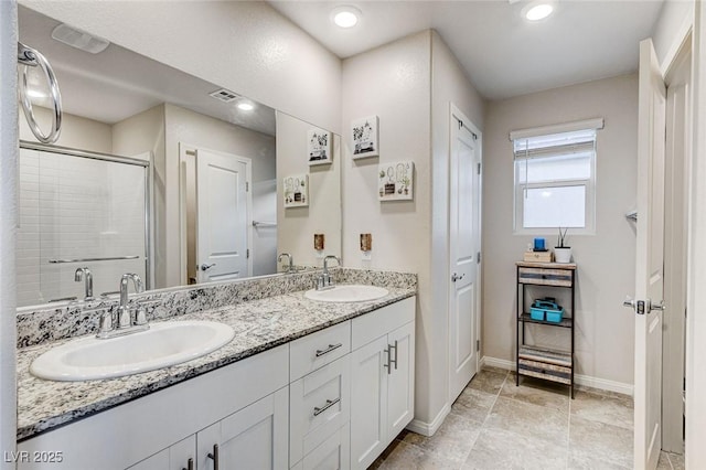 full bathroom with a sink, double vanity, a stall shower, and baseboards