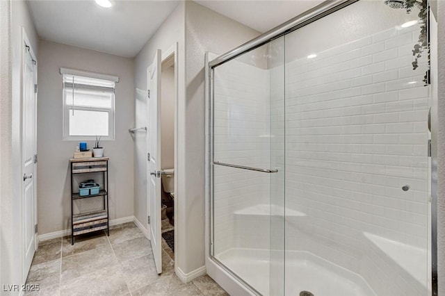 bathroom with a stall shower, toilet, and baseboards