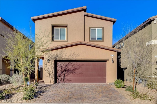 view of front of house with a tiled roof, decorative driveway, a garage, and stucco siding