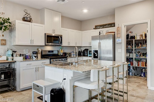 kitchen featuring a sink, light stone counters, a kitchen breakfast bar, appliances with stainless steel finishes, and white cabinets