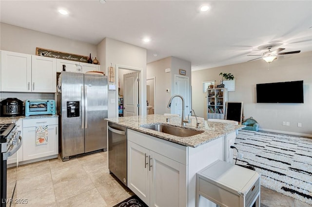 kitchen with a ceiling fan, a sink, light stone counters, appliances with stainless steel finishes, and white cabinets