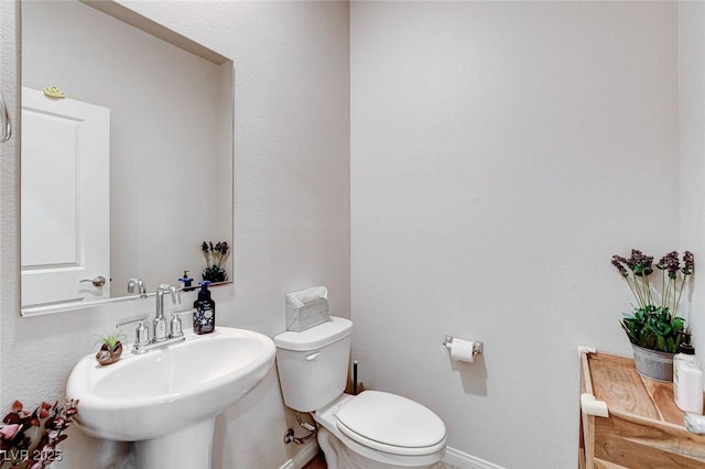 bathroom featuring baseboards, toilet, and a sink