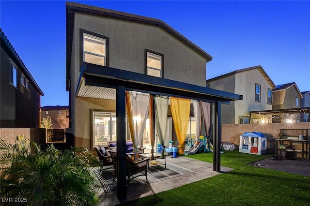 rear view of house with a yard, stucco siding, a patio, and fence