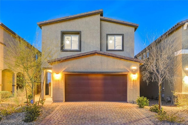 view of front facade with decorative driveway, a tiled roof, an attached garage, and stucco siding