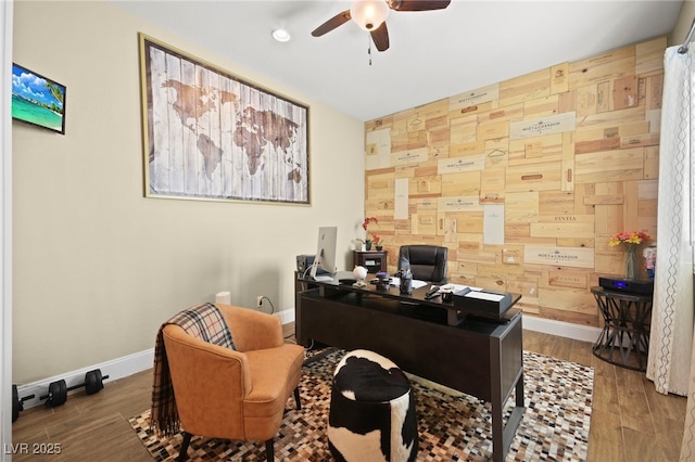 home office with wood finished floors, wooden walls, a ceiling fan, and baseboards