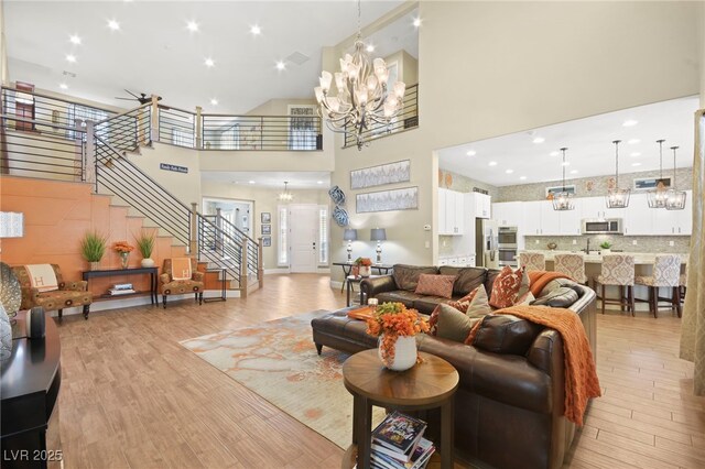 living area featuring a chandelier, light wood finished floors, stairs, and a towering ceiling