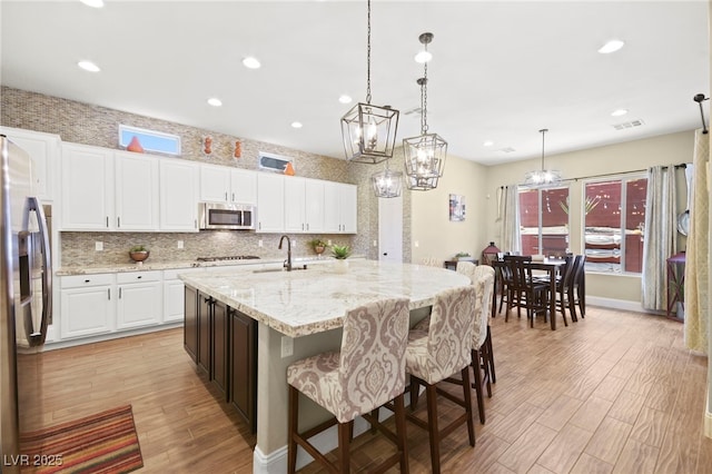 kitchen with a center island with sink, light wood-type flooring, appliances with stainless steel finishes, white cabinetry, and tasteful backsplash