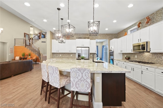 kitchen featuring a chandelier, light wood-type flooring, appliances with stainless steel finishes, white cabinets, and a sink