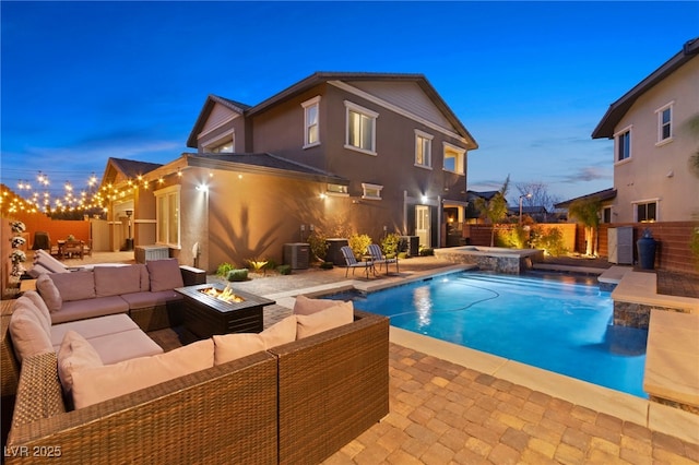 pool at dusk with a patio, central AC, an outdoor living space with a fire pit, a fenced in pool, and an in ground hot tub