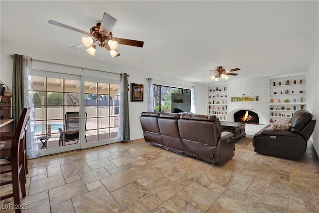 living room with built in features, a brick fireplace, stone tile flooring, and ceiling fan