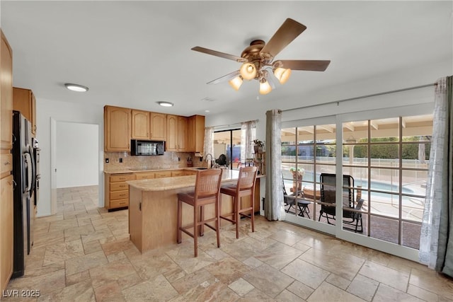 kitchen featuring stone tile floors, decorative backsplash, a breakfast bar, light countertops, and black microwave