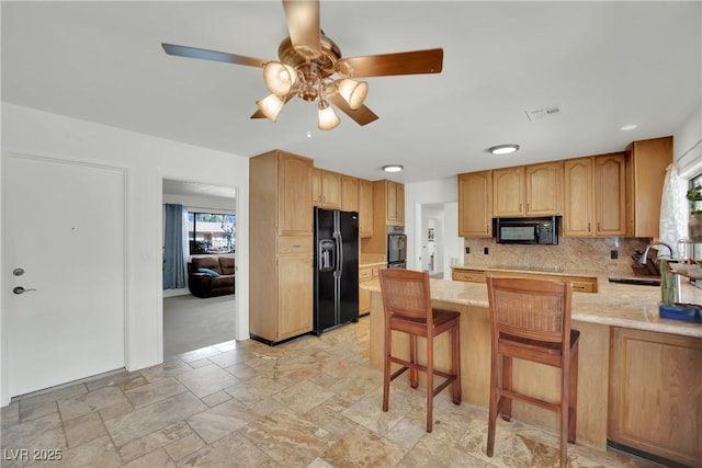 kitchen with stone tile floors, a peninsula, a sink, black appliances, and tasteful backsplash