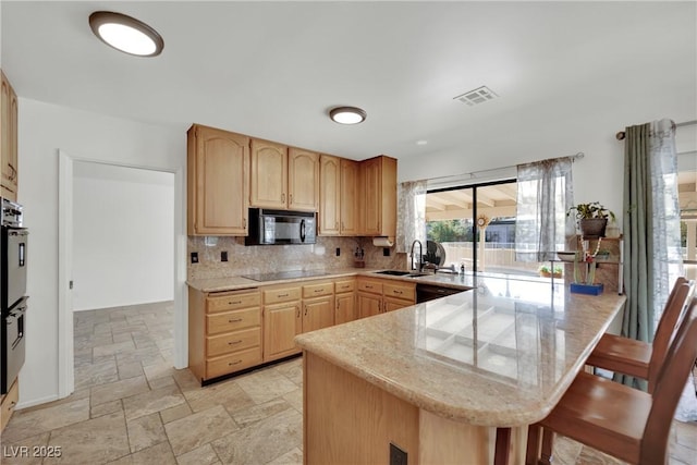 kitchen with black appliances, a breakfast bar, stone tile flooring, and light brown cabinetry